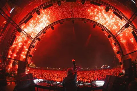 DJ z uniesioną pięścią na tle tłumu i fajerwerków. Niezapomniany sunrise lineup na festiwalu.