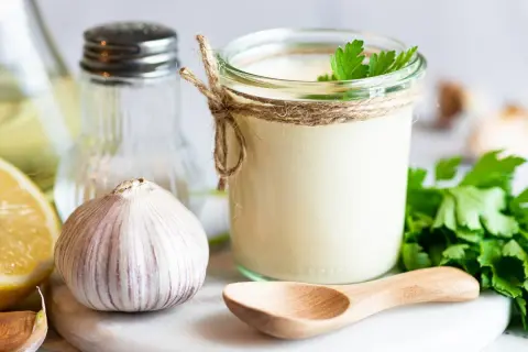 Słoik domowego aioli, czosnek, cytryna i natka pietruszki – składniki idealnego sosu.
