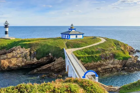 Faro y casa azul en una isla verde, conectada por un puente blanco sobre el mar Cantábrico en Lugo.
