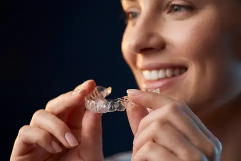 Donna sorridente tiene in mano allineatori dentali trasparenti, pronti per un sorriso perfetto.