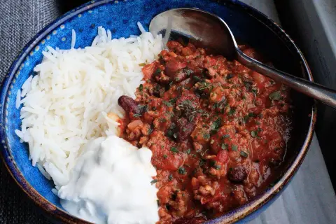 En blå skål med ris, en klick gräddfil och en portion av det godaste chili con carne, toppad med persilja.