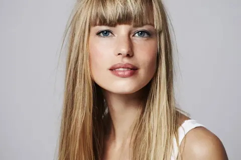 Blonde Frau mit blauen Augen und einem leichten Lächeln. Sie fragt sich, wie oft Haare blondieren für diesen Look nötig ist.