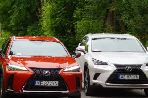 Dwa modele Lexus SUV: czerwony UX i biały NX, zaparkowane na tle zieleni.