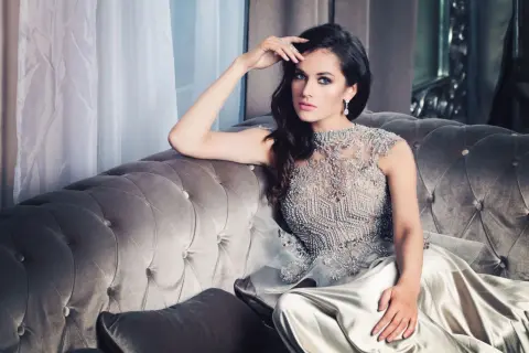 Elegancka kobieta w sukni w stylu glamour, ozdobionej kryształkami, siedzi na aksamitnej kanapie.