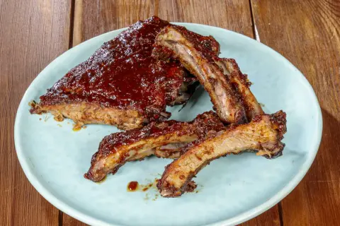 Succulente costine di maiale glassate con salsa barbecue, servite su un piatto azzurro su un tavolo di legno.