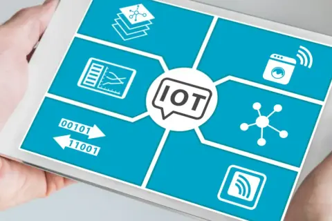 Tablet pokazuje schemat przemysłowego internetu rzeczy (IoT) z ikonami symbolizującymi dane, połączenia i urządzenia.