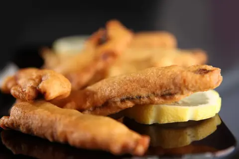 Beignets de sardines dorés et croustillants, servis avec des rondelles de citron sur une assiette noire.