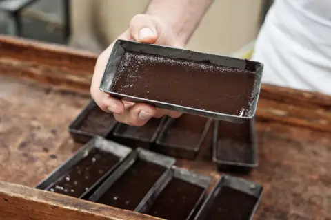 Mani esperte versano cioccolato lavorato a freddo in stampini metallici, pronti per diventare delizie artigianali.