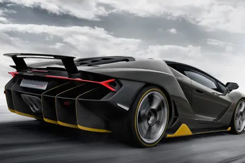 Czarny Lamborghini Centenario z żółtymi akcentami pędzi po drodze, chmury na niebie podkreślają dynamikę.