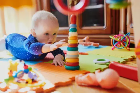 Dziecko bawi się kolorowymi, potencjalnie niebezpiecznymi zabawkami dla dzieci, takimi jak wieża z kółek i spiralna kula.