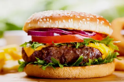 Soczysty burger z serem, pomidorem, czerwoną cebulą i sałatą na bułce z sezamem.