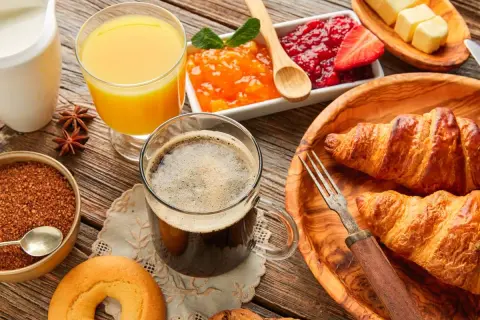 Pyszne śniadanie kontynentalne: świeże croissanty, dżemy, masło, kawa i sok pomarańczowy na drewnianym stole.