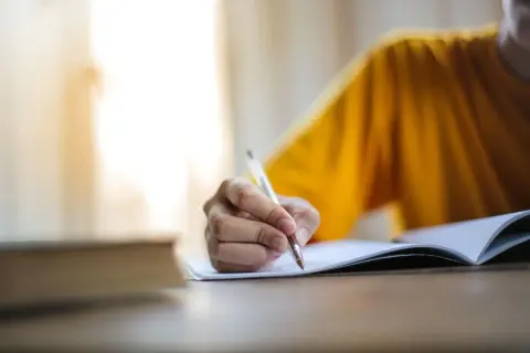 Main d'une personne écrivant dans un cahier, peut-être pour l'archive des noms de famille algériens.