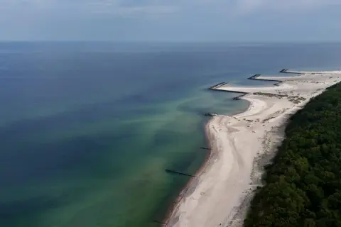 Plaża w Jarosławcu, zwana czasem "plażą dubaj", z kamiennymi falochronami i zielonym lasem.