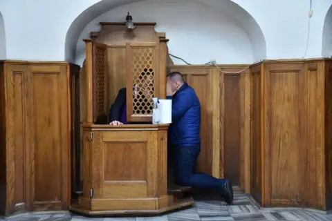 Mężczyzna klęczy przy konfesjonale, zasłaniając twarz. Czy w kościele anglikańskim jest spowiedź?