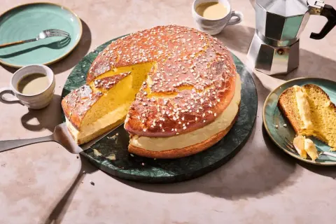 Eine köstliche Tarte Tropezienne, aufgeschnitten und mit einer Kaffeetasse und einem Moka-Topf serviert.