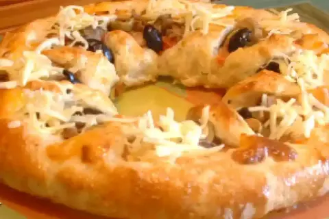 Pizza maison avec une croûte dorée, garnie d'olives noires et de fromage râpé. Parfait pour une recette pâte à pizza rapide.