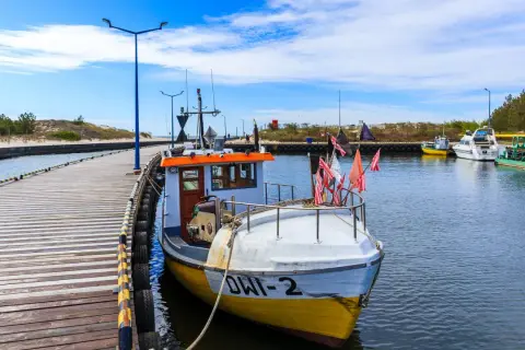 Port w Dźwirzynie, z łodzią rybacką przy drewnianym pomoście, zaprasza na morskie przygody. Atrakcje czekają!