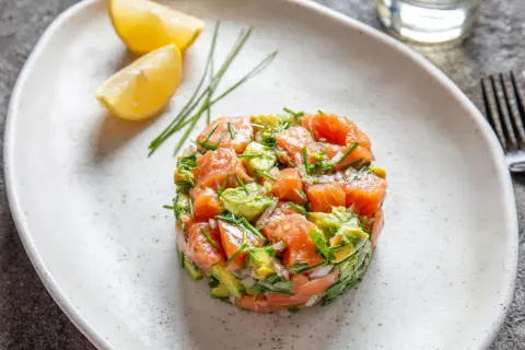 Un délicieux tartare de saumon frais, mélangé à de l'avocat et des herbes, servi avec des quartiers de citron.