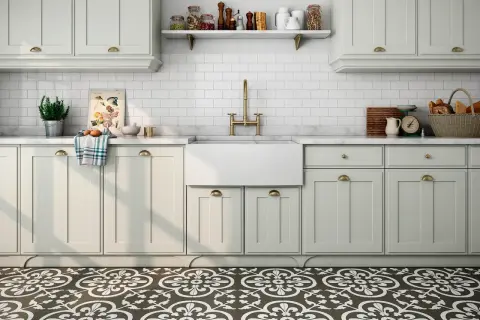 Cocina con suelo hidráulico de diseño floral. Encimera de mármol, fregadero blanco, grifería dorada y armarios claros.