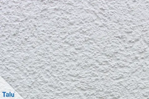 Nahaufnahme einer weißen, strukturierten Wand, die zeigt, wie man eine Wand verputzt. Das Korn ist unregelmäßig und erzeugt eine interessante Textur.