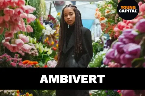 Een jonge vrouw met vlechten staat tussen bloemen. De tekst "AMBivert" suggereert de betekenis van ambivert: iemand die zowel extravert als introvert is.