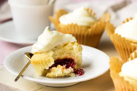 En närbild på en cupcake med vit frosting och en härlig röd fyllning. Flera liknande cupcakes med fyllning syns i bakgrunden.