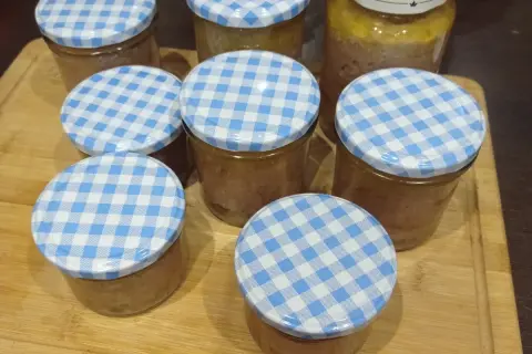 Mehrere Gläser mit selbstgemachter Leberwurst, verschlossen mit blau-weißen Karodeckeln, stehen auf einem Holzbrett.