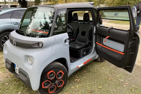 Citroën Ami, un quadriciclo elettrico compatto, con porte aperte e interni visibili. Il suo design unico e le dimensioni ridotte lo rendono perfetto per la città.