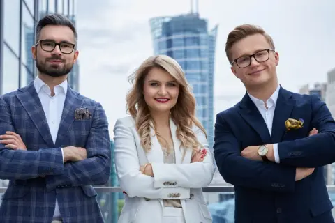 Trzy osoby w eleganckich strojach biznesowych stoją na tle nowoczesnych budynków.