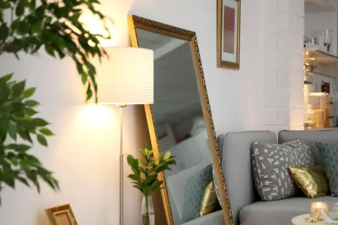 Ein großer Spiegel und eine Stehlampe helfen, die dunkle Wohnung heller zu machen. Ein Sofa mit Kissen und eine Pflanze vervollständigen die Szene.