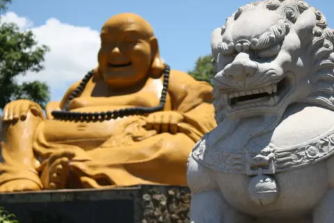 Złoty Budda i kamienna lwica strażniczka na tle błękitnego nieba.