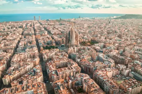 Widok z lotu ptaka na Eixample w Barcelonie, z Sagradą Familią górującą nad miastem i morzem w tle.
