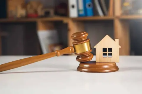 Richterhammer und Holzhaus-Modell auf einem Tisch, symbolisch für ein Immobilien-Bieterverfahren.
