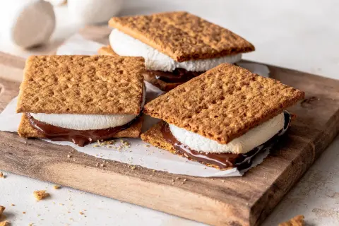 Drei S'mores Cookies mit geschmolzener Schokolade und Marshmallows auf einem Holzbrett.