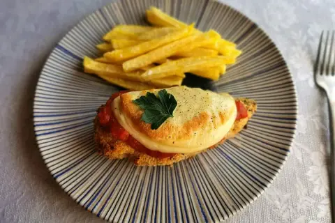 Delicioso pollo a la parmesana con papas fritas crujientes, servido en un plato rayado.