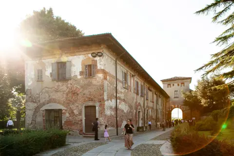Passeggiata serale all'abbazia di Chiaravalle, con edifici storici in mattoni e un arco d'ingresso illuminato dal sole.