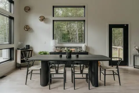 Mesa de comedor moderna con sillas de madera y asientos de mimbre. Un jarrón blanco y dos candelabros negros decoran la mesa, perfecta para decorar mesa comedor.