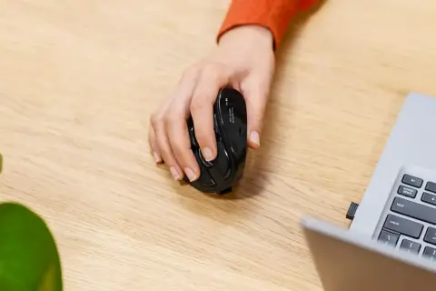 Mano sujetando un ratón negro, listo para usarlo y desbloquear el ratón del portátil.