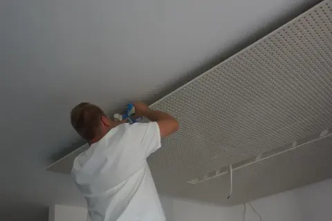 Mężczyzna montuje płyty karton gips na suficie w nieogrzewanym domu.