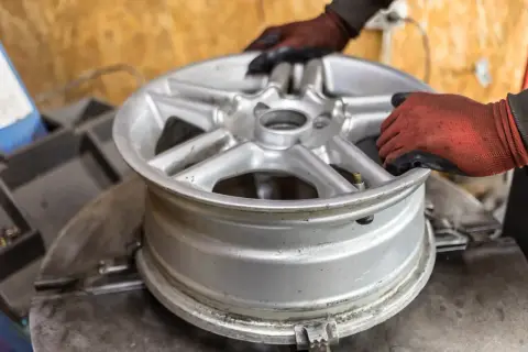 Ręce w rękawiczkach ustawiają aluminiową felgę na maszynie. Zastanawiasz się, ile kosztuje prostowanie felg?
