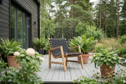 En modern fåtölj med trästomme och flätad sits i plast står på en altan omgiven av grönska.