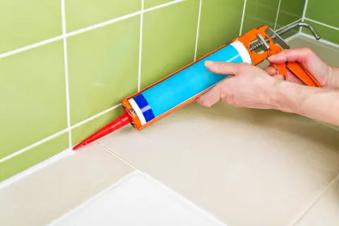 Application d'un nouveau joint blanc avec un pistolet à silicone pour refaire le joint de douche.