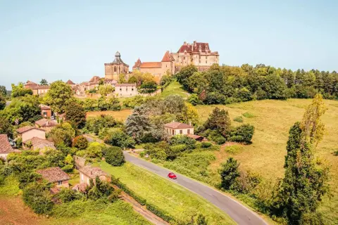 Un village pittoresque en France, idéal pour savoir où partir en France en mai. Un château domine la colline verdoyante.