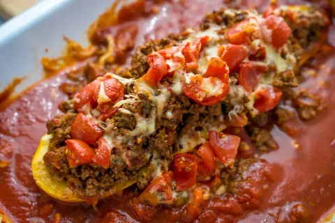 Herzhafte zucchini schiffchen gefüllt mit Hackfleisch, Tomaten und Käse, in einer roten Sauce.