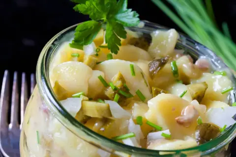 Ein köstlicher Kartoffelsalat ohne Mayo, mit Gurkenstücken und frischem Schnittlauch garniert, serviert in einem Glas.