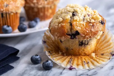 Saftige Blaubeermuffins mit Streuseln, perfekt für ein Blaubeermuffins Rezept. Frische Blaubeeren liegen daneben.