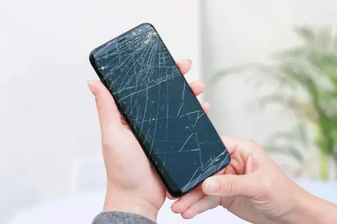Dwie dłonie trzymają pęknięty telefon, czekając na wymianę dotyku.