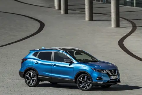 Niebieski Nissan Qashqai+2 zaparkowany na placu z betonowymi kolumnami i krętymi ścieżkami.