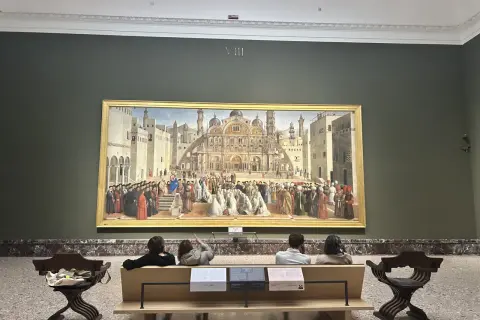 A grand painting depicting a historical scene is the centerpiece of this art in Milan gallery. Visitors sit on a bench, contemplating the detailed artwork.